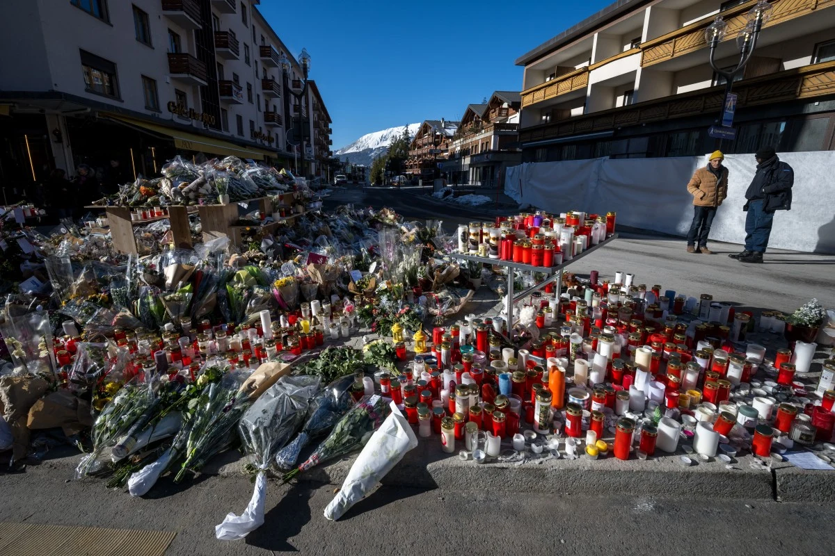 Morze kwiatów i zniczy nieopodal miejsca tragedii. W szwajcarskim barze Le Constellation w noc sylwestrową zmarło 40 osób Tłumy zniczy i kwiatów ustawionych na chodniku oraz bliskiej ulicy, stanowiących miejsce pamięci lub hołdu, widoczne dwie osoby przyglądające się z oddali, w tle góry oraz zabudowania miejskie.