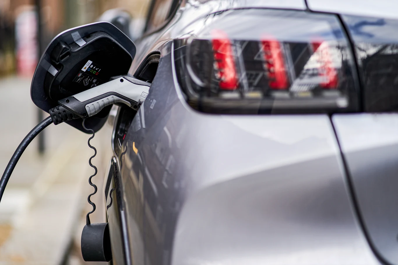 Prezes Peugeota szczerze o przyszłości marki. Deklaracje mogą zaskoczyć Proces ładowania elektrycznego samochodu za pomocą kabla, widoczne tylne światła pojazdu oraz szczegóły wtyczki podłączonej do portu ładowania.