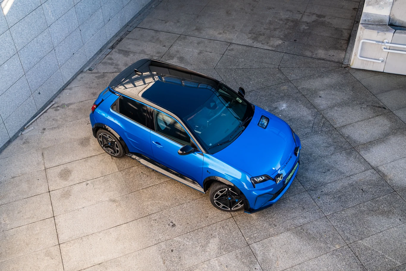 Niebieski samochód osobowy stojący na betonowej powierzchni, ujęcie wykonane z góry, auto posiada przeszklony dach, czarne felgi oraz elementy chromowane.