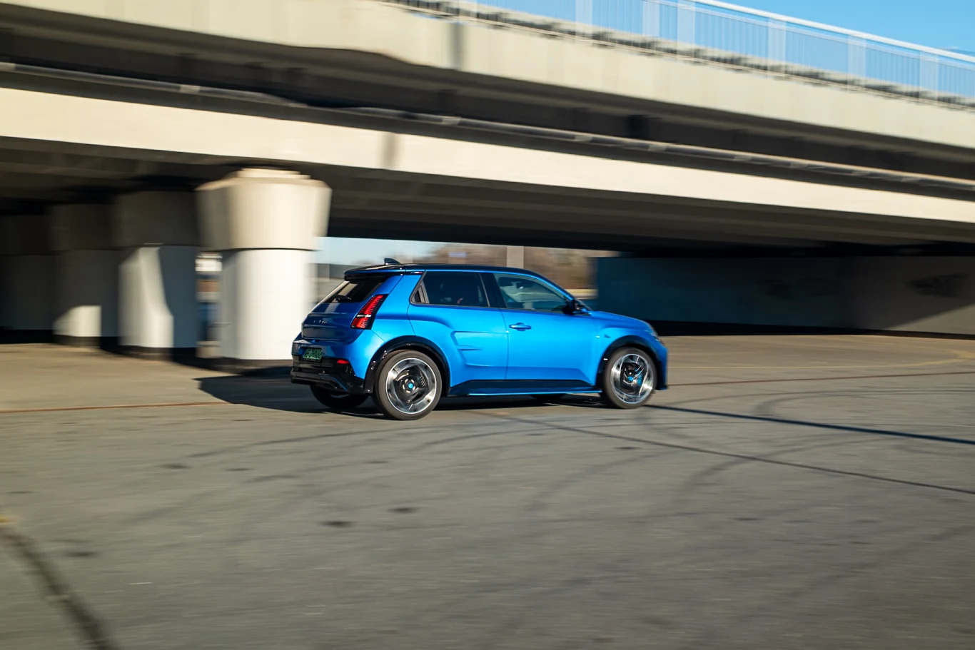 Nowoczesny niebieski samochód osobowy w ruchu, poruszający się pod betonowym wiaduktem na szerokiej, pustej drodze.