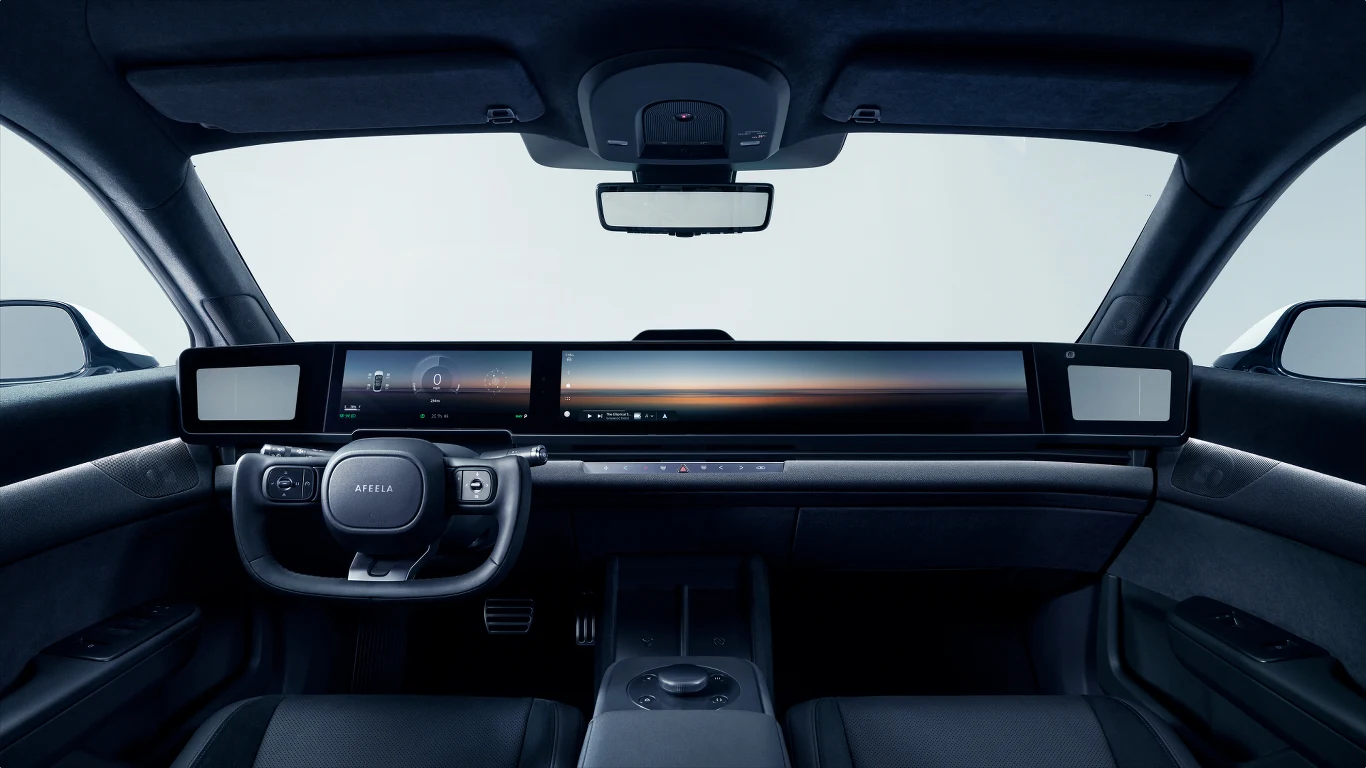 Przyciski funkcyjne w Afeeli 1 ograniczone zostały do minimum Nowoczesne wnętrze samochodu elektrycznego z panoramicznym cyfrowym panelem sterowania, minimalistyczną deską rozdzielczą oraz sportową kierownicą, wszystko w ciemnej kolorystyce.