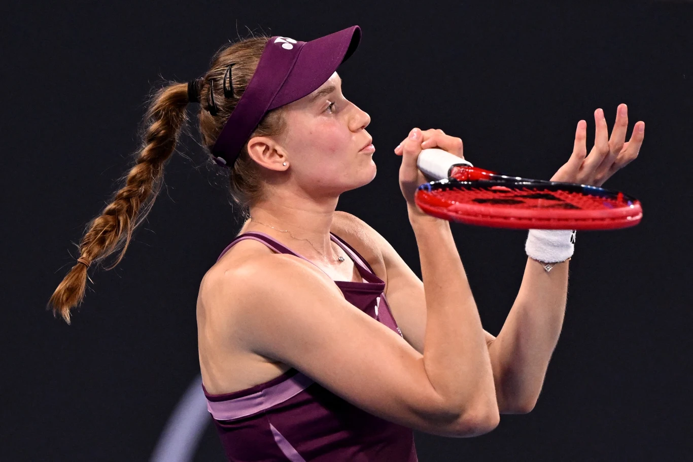 Tenisistka w sportowym stroju w trakcie serwowania piłki, skupiona na wykonaniu perfekcyjnego ruchu, z uniesioną rakietą i piłką tenisową unoszącą się w powietrzu.