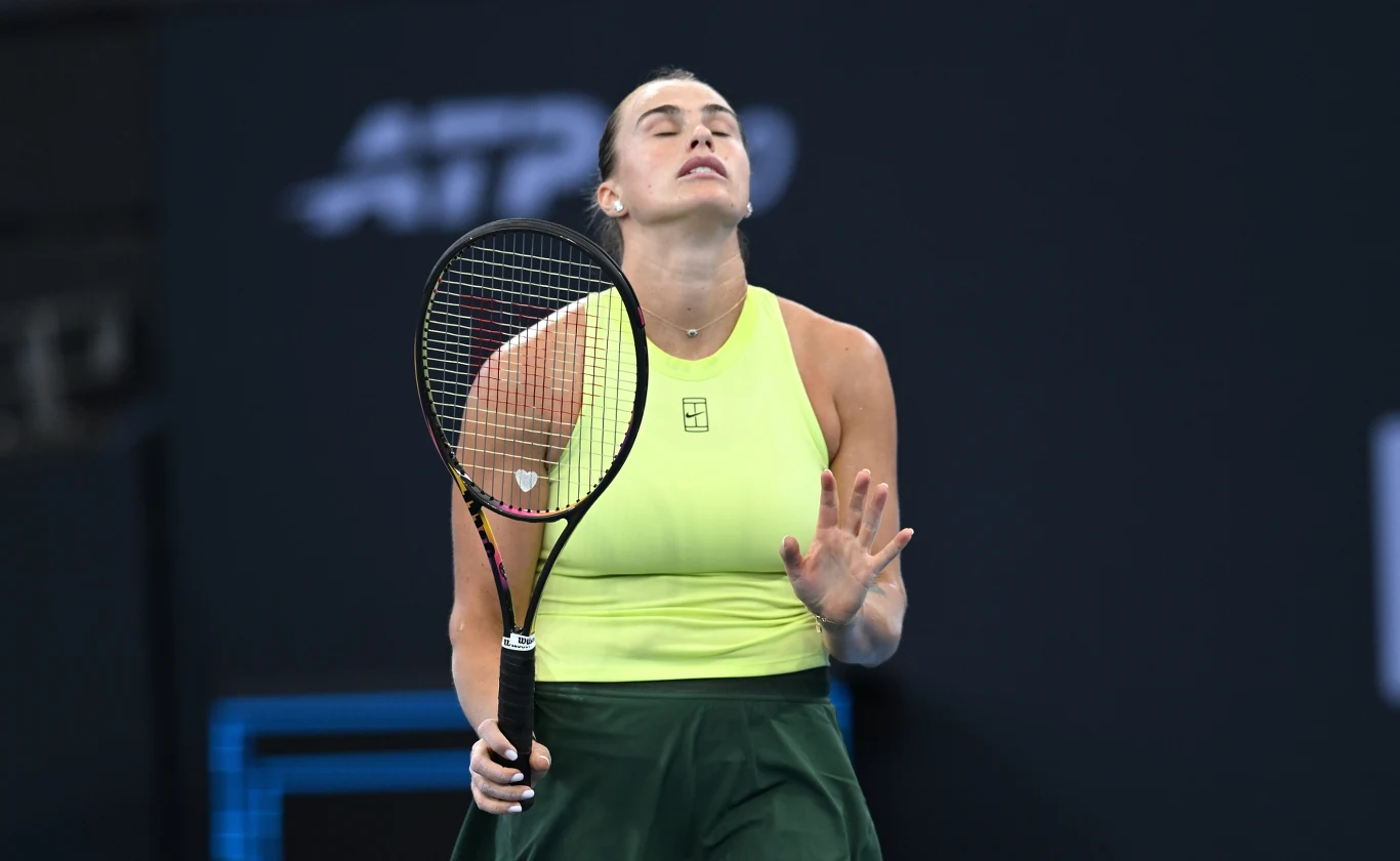 Aryna Sabalenka, Brisbane 2026 Tenisistka ubrana w jasnozielony top i ciemnozieloną spódnicę, trzymająca rakietę, wyraża frustrację z zamkniętymi oczami i uniesioną dłonią podczas meczu na korcie.