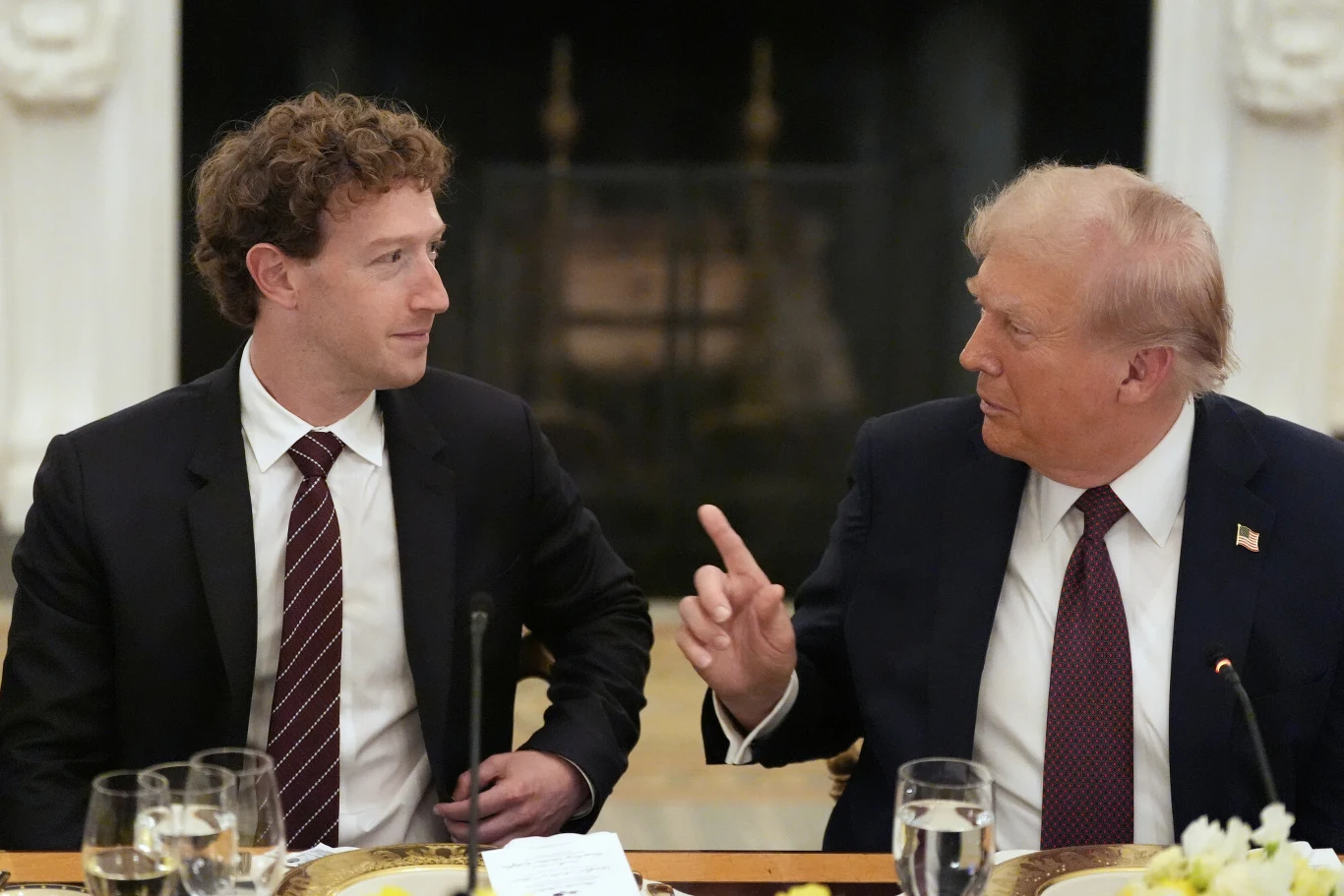 Szef Meta Mark Zuckerberg i prezydent USA Donald Trump Dwóch mężczyzn w garniturach siedzi przy stole, prowadząc rozmowę, na stole znajdują się naczynia z jedzeniem oraz kieliszki.