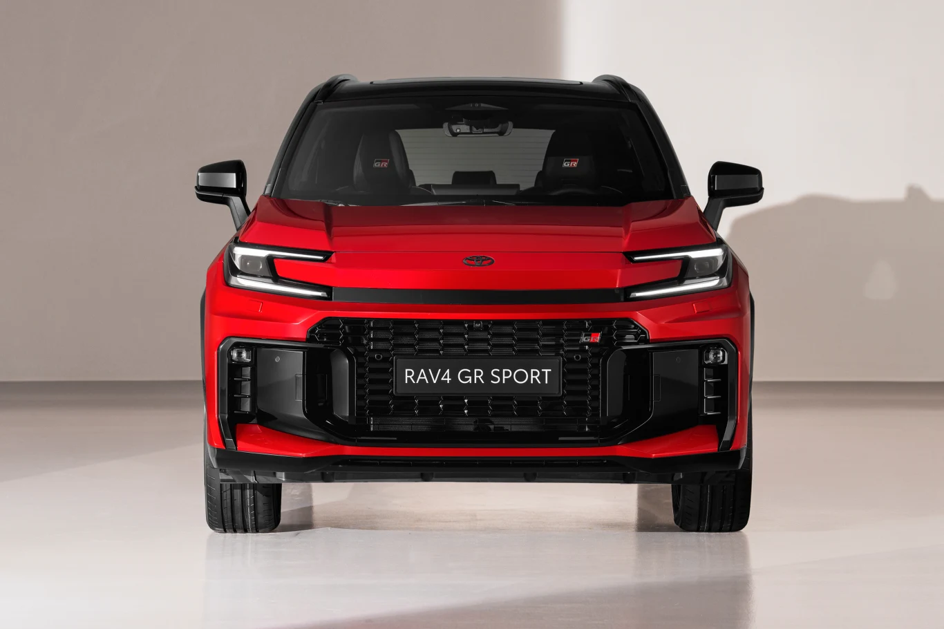 Czerwony samochód Toyota RAV4 GR SPORT ustawiony na białym tle, widok od frontu z wyeksponowaną atrapą chłodnicy, charakterystycznymi reflektorami LED i sportowymi detalami stylistycznymi.