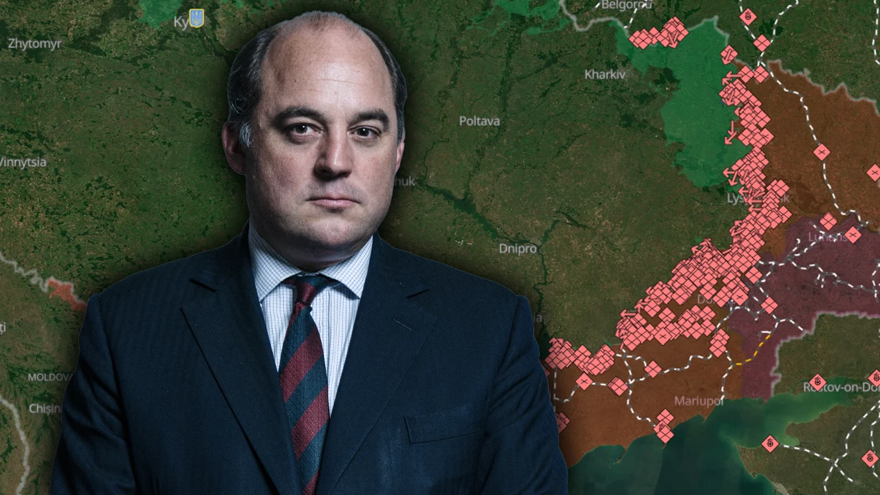 Były minister obrony Wielkiej Brytanii o koalicji chętnych Mężczyzna w garniturze stoi na tle szczegółowej mapy przedstawiającej front wojenny z zaznaczonymi konfliktami i liniami walk.