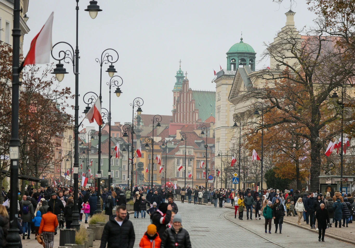 Warszawa została wyróżniona przez dziennik "The New York Times" Tłum ludzi spacerujących po szerokiej ulicy w centrum miasta, liczne lampy ozdobione polskimi flagami, w tle kamienice oraz kościół z charakterystyczną zieloną kopułą, atmosfera święta lub ważnego wydarzenia narodowego.