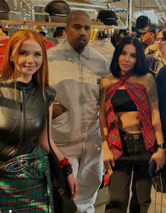 Trzy osoby pozujące razem w sklepie odzieżowym, dwie kobiety w nowoczesnych stylizacjach z motywami szkockiej kraty oraz mężczyzna w jasnym ubraniu, wokół w tle widoczna jest odzież na półkach oraz kilka innych osób.