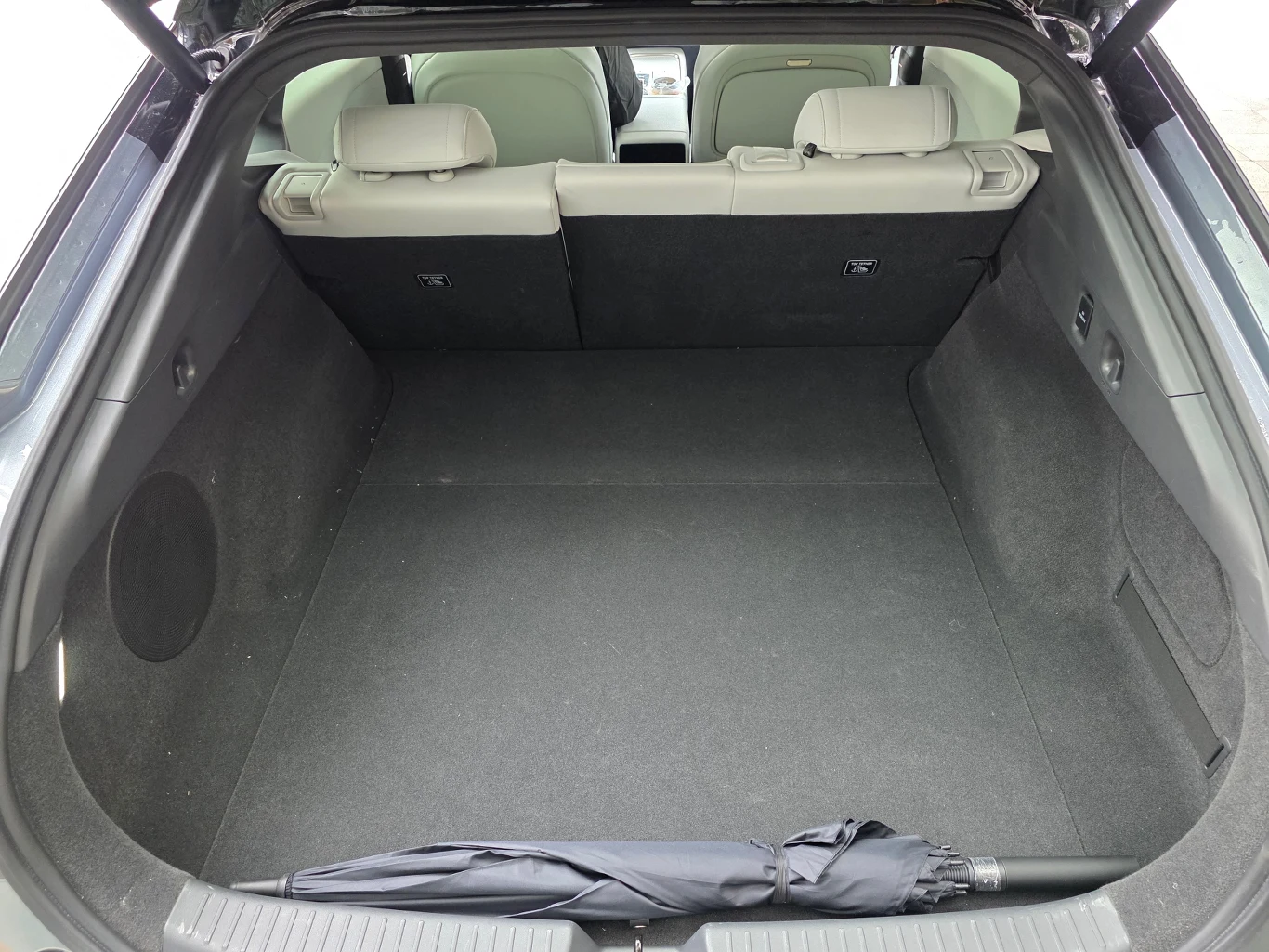 Wnętrze bagażnika samochodu osobowego z rozłożoną tylną kanapą w jasnej tapicerce, na podłodze bagażnika leży czarny złożony parasol.