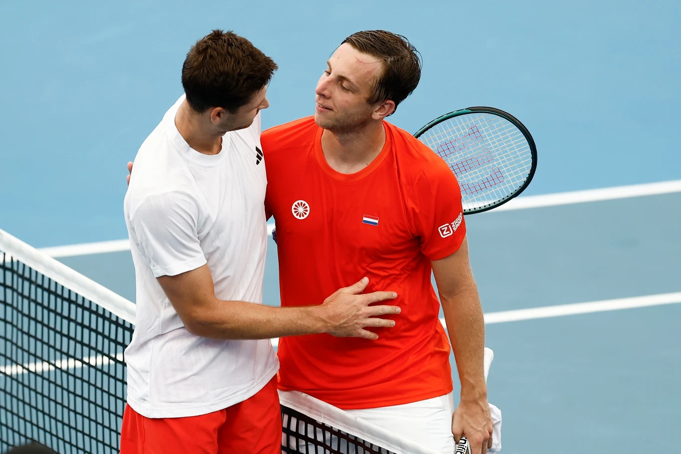 Hubert Hurkacz i Tallon Griekspoor Dwóch tenisistów przy siatce podaje sobie ręce i wymienia uprzejmości po zakończonym meczu tenisowym. Jeden z nich ubrany jest na czerwono, drugi na biało, obaj stoją na korcie tenisowym.