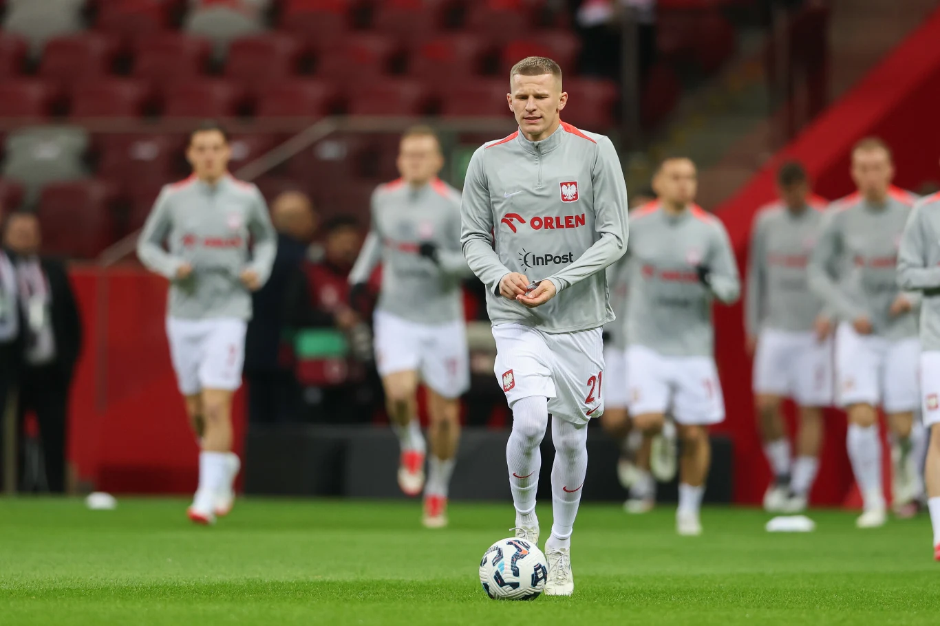 Piłkarze reprezentacji Polski w szarych strojach sportowych podczas rozgrzewki na stadionie, na pierwszym planie zawodnik z piłką.