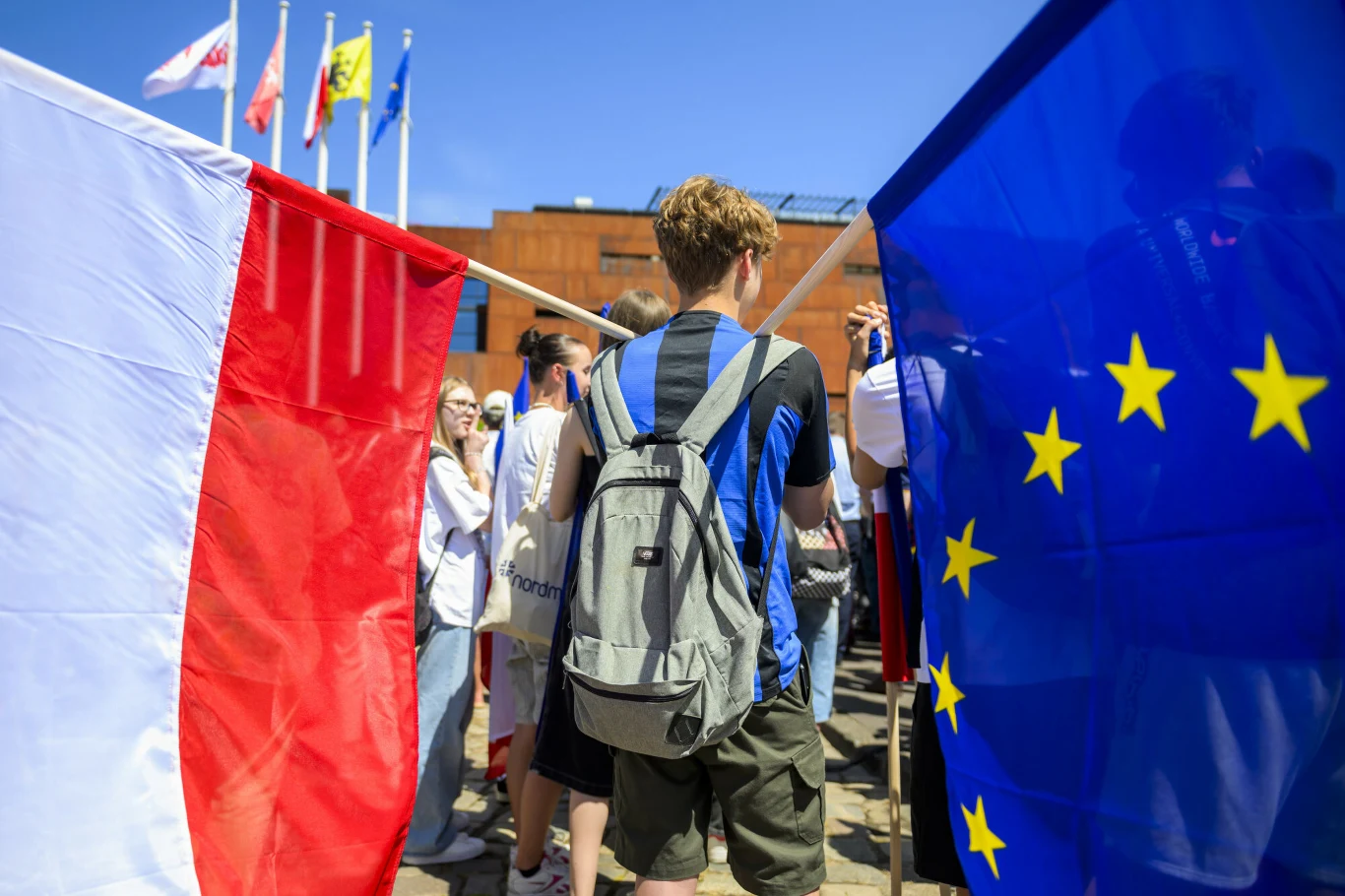 Nowy sondaż na temat polexitu. Zdj. ilustracyjne Młody Polak sfotografowany od tyłu trzyma na ramionach dwie flagi - z lewej polską, z prawej Unii Europejskiej.