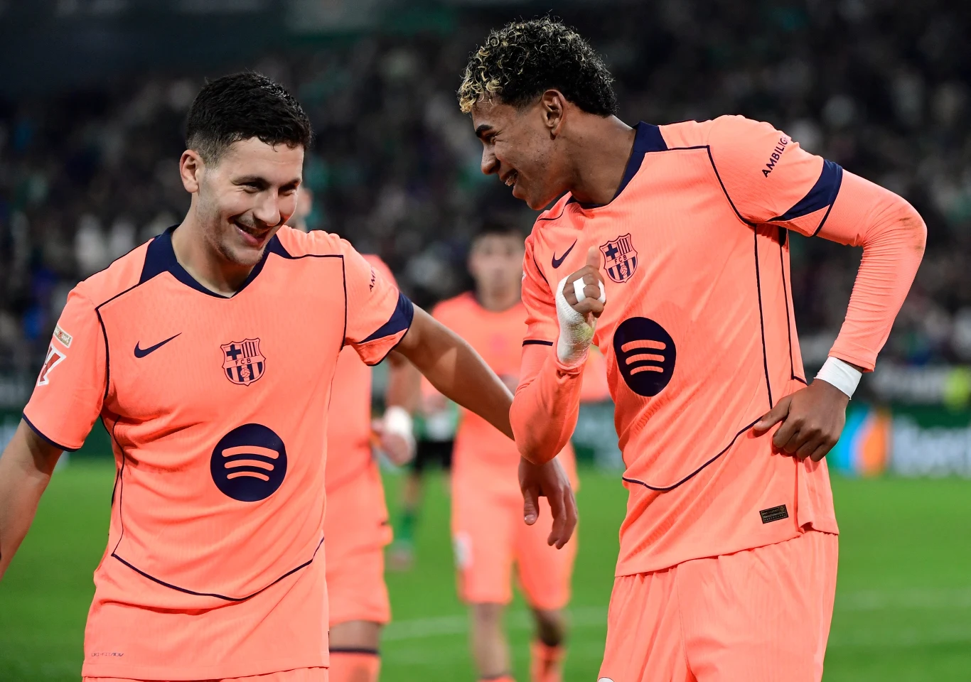 Dwóch piłkarzy drużyny FC Barcelona ubranych w różowe stroje śmieje się i rozmawia ze sobą na murawie podczas meczu.