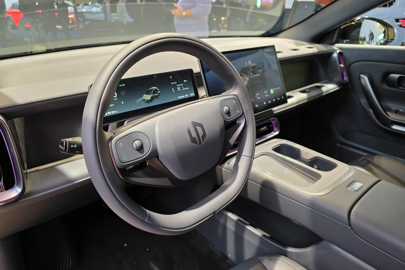 Nowoczesne wnętrze samochodu elektrycznego z dużym panelem dotykowym centralnym i elektronicznym zestawem wskaźników. Minimalistyczne wykończenie, wygodne fotele oraz mnogość schowków i portów USB. Skupienie na innowacyjnej technologii i ergonomii.