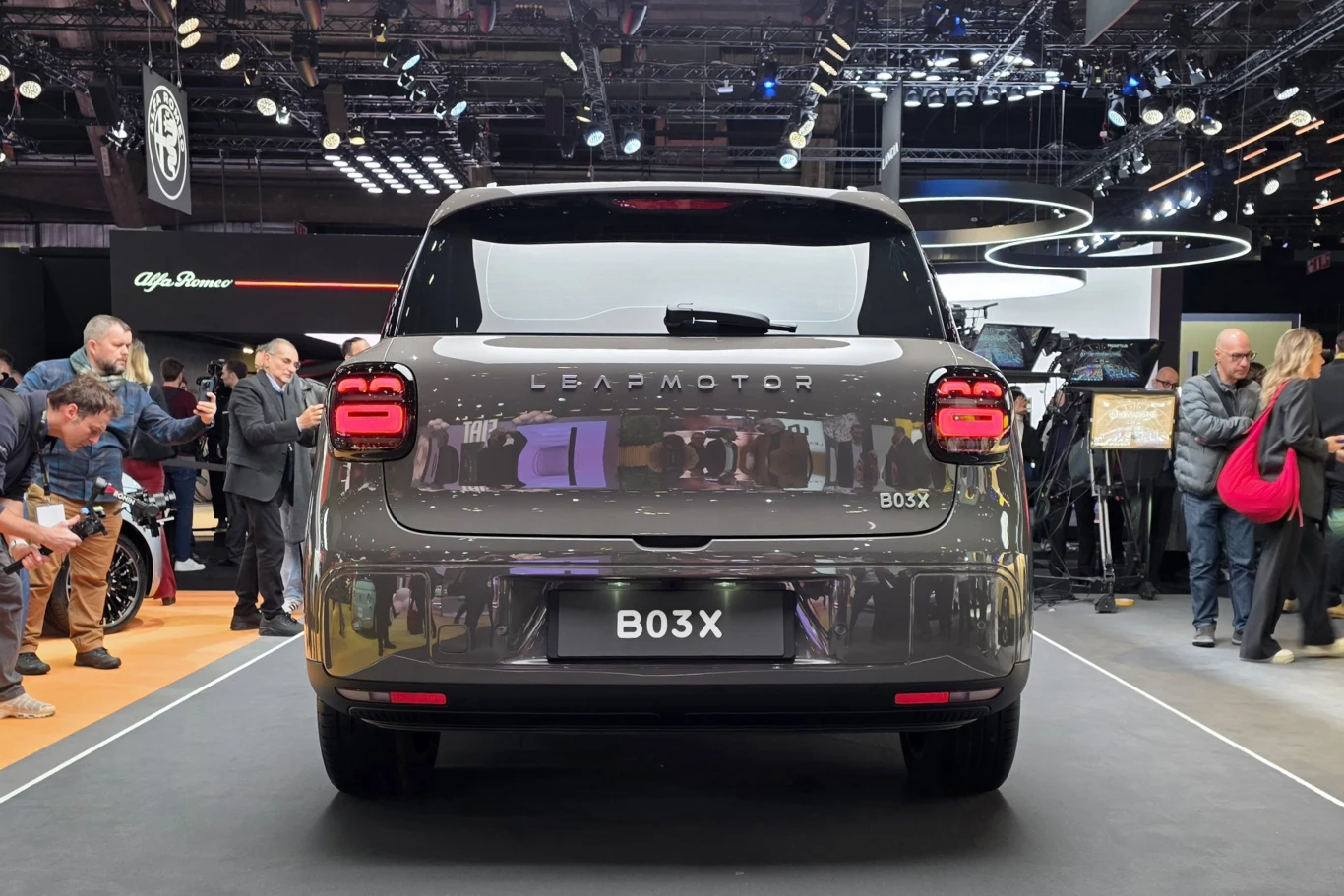 Nowoczesny szary samochód marki Leapmotor model BO3X zaprezentowany na targach motoryzacyjnych, wokół pojazdu zgromadzeni są ludzie oraz dziennikarze obserwujący prezentację auta w jasnym oświetleniu ekspozycyjnym.