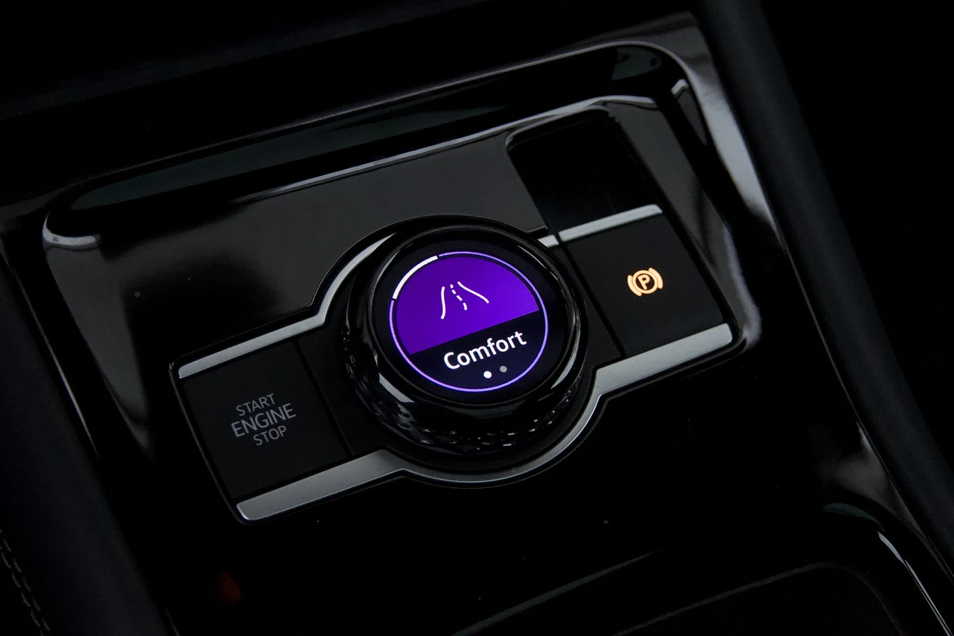 Centralny panel samochodowy z pokrętłem trybu jazdy ustawionym na Comfort, przyciskiem uruchamiania silnika oraz symbolem elektronicznego hamulca postojowego.