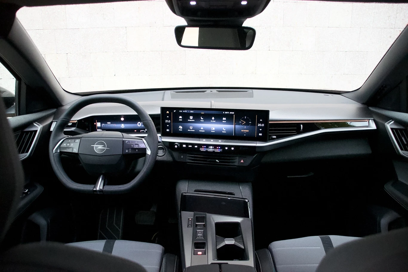 Nowoczesne wnętrze samochodu marki Opel z cyfrowym kokpitem, dużym dotykowym ekranem na środku deski rozdzielczej oraz wielofunkcyjną kierownicą. Fotele pokryte tapicerką o sportowym charakterze, wykończenia w odcieniach czerni i srebra.