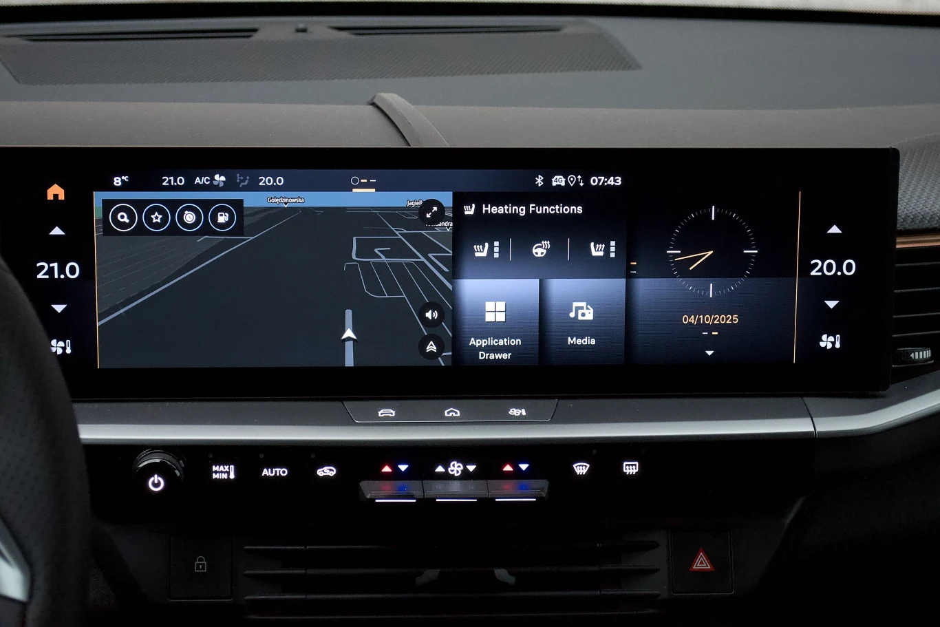 Cyfrowy kokpit samochodu z szerokim ekranem dotykowym, na którym wyświetlają się aplikacje multimedialne, system nawigacji GPS oraz ustawienia klimatyzacji i godzina.