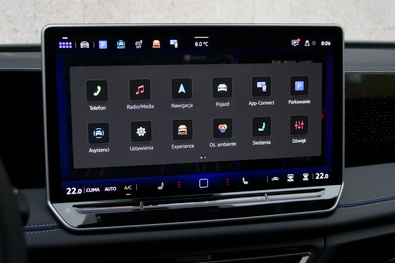 Dotykowy ekran samochodowego systemu multimedialnego z wyraźnie widocznym interfejsem i ikonami różnych funkcji, takich jak telefon, radio, nawigacja, ustawienia klimatyzacji oraz opcje multimedialne.