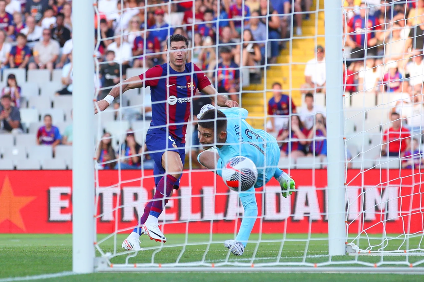 Robert Lewandowski w rywalizacji z Tottenhamem w 2023 roku Piłkarz w granatowo-bordowym stroju oddaje strzał na bramkę podczas meczu, bramkarz w niebieskim stroju próbuje obronić piłkę, na trybunach widoczni kibice.