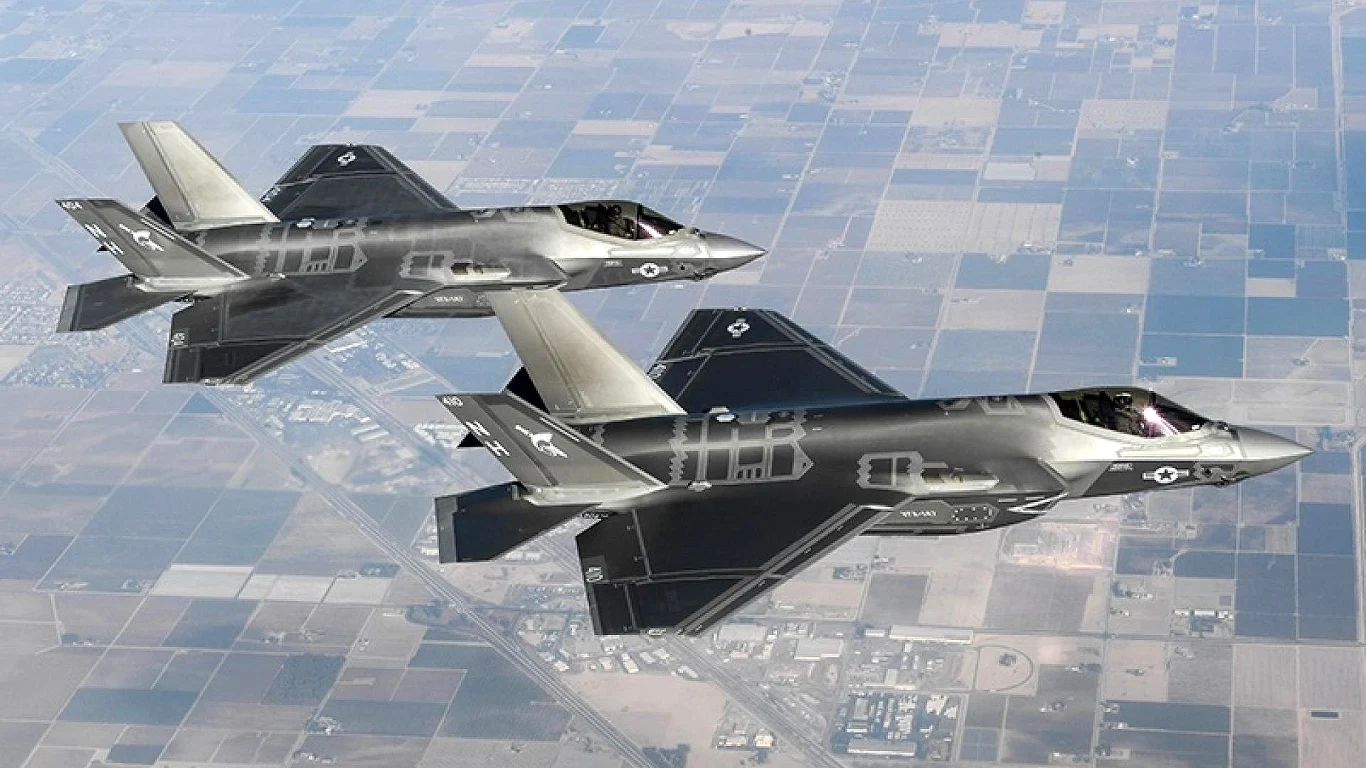 USA zbudowały rekordową liczbę myśliwców F-35. Szykują się do wojen Dwa nowoczesne myśliwce wojskowe w barwach sił powietrznych lecące obok siebie na dużej wysokości nad rozległymi polami rolniczymi, poniżej widoczna siatka pól i dróg.