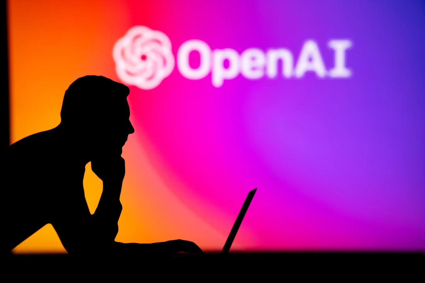 Giganci technologiczni apelują o wzmocnienie systemów cyberbezpieczeństwa w obawie przed AI Sylwetka osoby przy laptopie, kolorowy ekran, duże logo OpenAI, temat cyberbezpieczeństwa i AI.