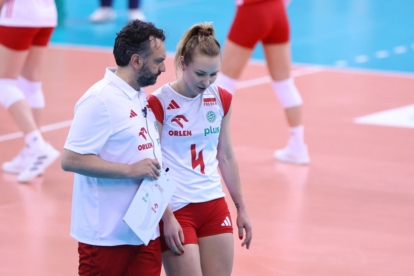 Marlena Kowalewska w rozmowie ze Stefano Lavarinim Siatkarz i trener drużyny narodowej Polski rozmawiają na boisku podczas przerwy w meczu siatkówki, oboje ubrani w biało-czerwone stroje sportowe.