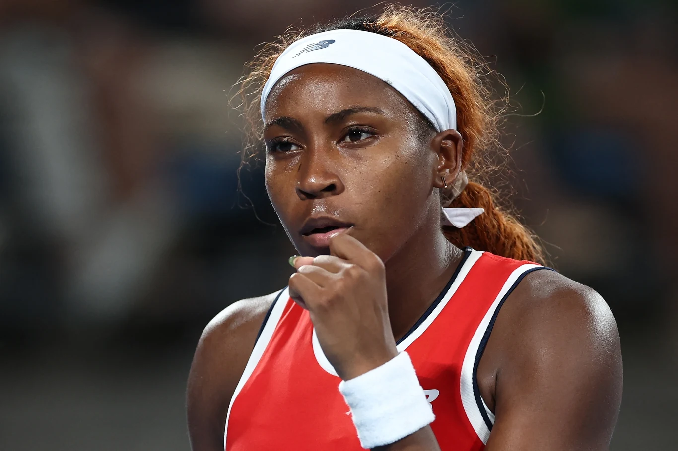 Młoda sportsmenka w stroju sportowym i opasce na głowie na tle rozmytego boiska, skoncentrowana i gotowa do rywalizacji.