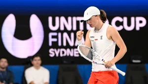 Tenisistka w białej czapce oraz stroju sportowym wykonuje gest triumfu, trzymając rakietę w ręce na tle napisu UNIted CUP FINAL Sydney, co sugeruje sportową rywalizację podczas ważnego turnieju tenisowego.