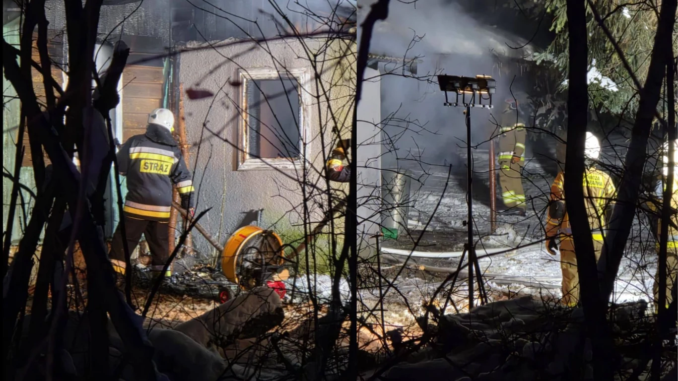 Jurków. Pożar pustostanu. Nie żyje mężczyzna Strażacy gaszący pożar w budynku, widoczny dym unoszący się z wnętrza, profesjonalny sprzęt gaśniczy oraz reflektory oświetlające teren akcji, otoczenie z gałęziami drzew i krzewów.
