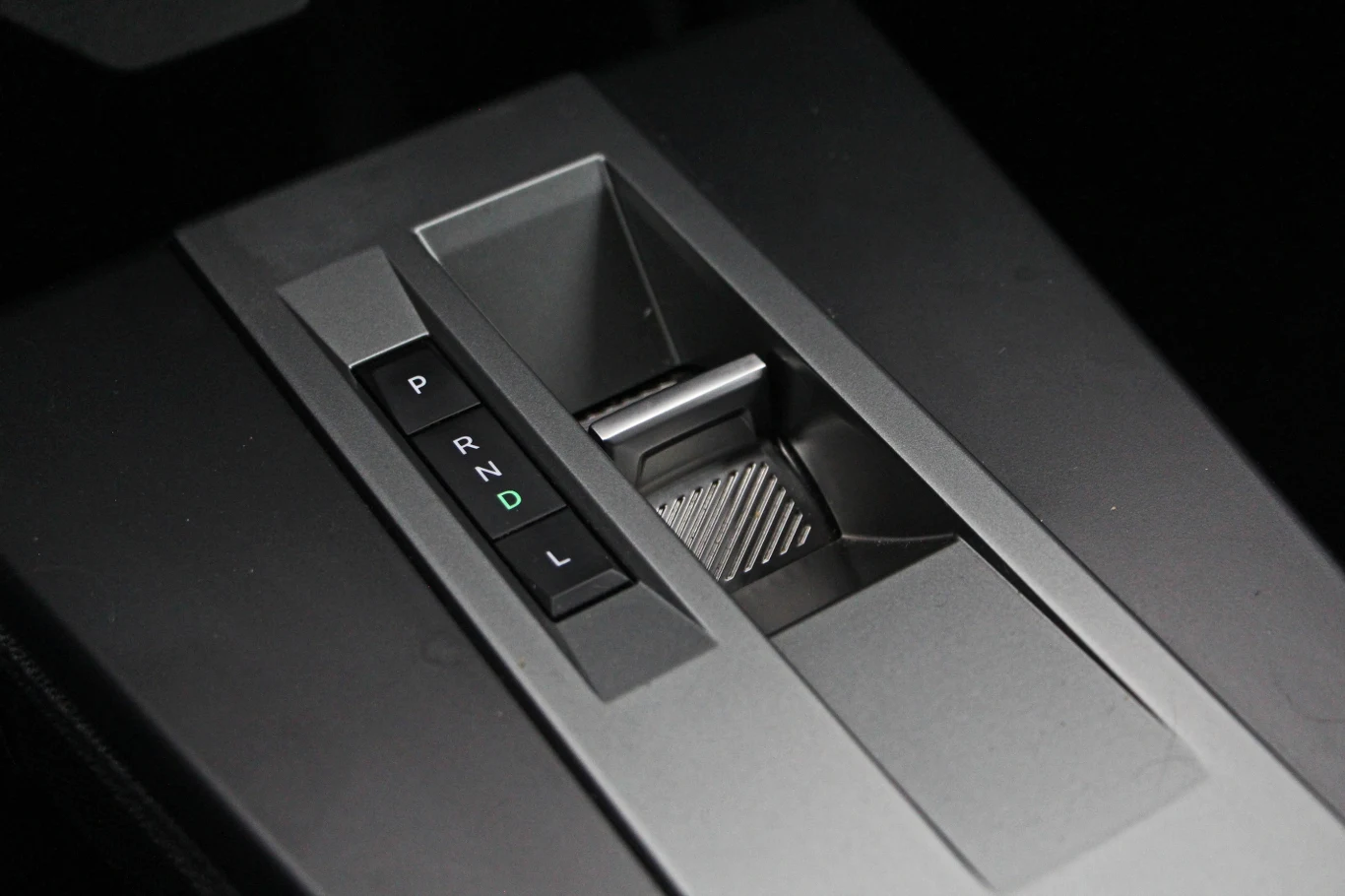 Panel automatycznej skrzyni biegów w samochodzie z widoczną dźwignią zmiany biegów oraz oznaczeniami P, R, N, D, L na czarnej, matowej powierzchni.