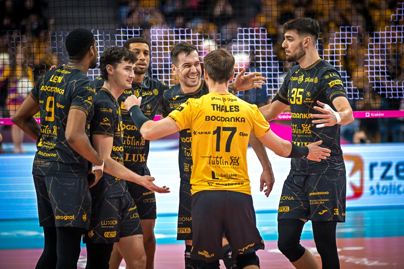 Siatkarze Bogdanki LUK Lublin, z prawej Kewin Sasak Grupa siatkarzy w żółto-czarnych strojach drużyny z napisem LUK Lublin celebruje udaną akcję na boisku, w tle widoczne trybuny i siatka.