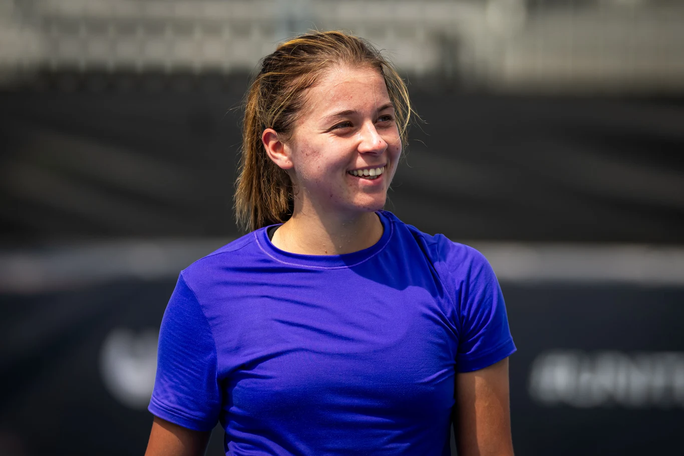 Maja Chwalińska rywalizowała o awans do drugiej rundy eliminacji Australian Open Uśmiechnięta młoda kobieta w fioletowej koszulce sportowej na tle rozmazanego stadionu.