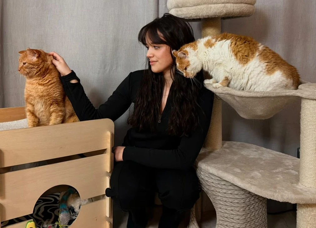 Maja Sznajdrowska poświęca cały swój wolny czas potrzebującym kotom. Jej niekończąca się pomoc urzekła internautów Kobieta w czarnym ubraniu siedzi obok dwóch rudych kotów. Jeden kot znajduje się na drapaku, a drugi stoi na drewnianym podwyższeniu. Tło stanowi zasłona oraz elementy wyposażenia dla kotów.