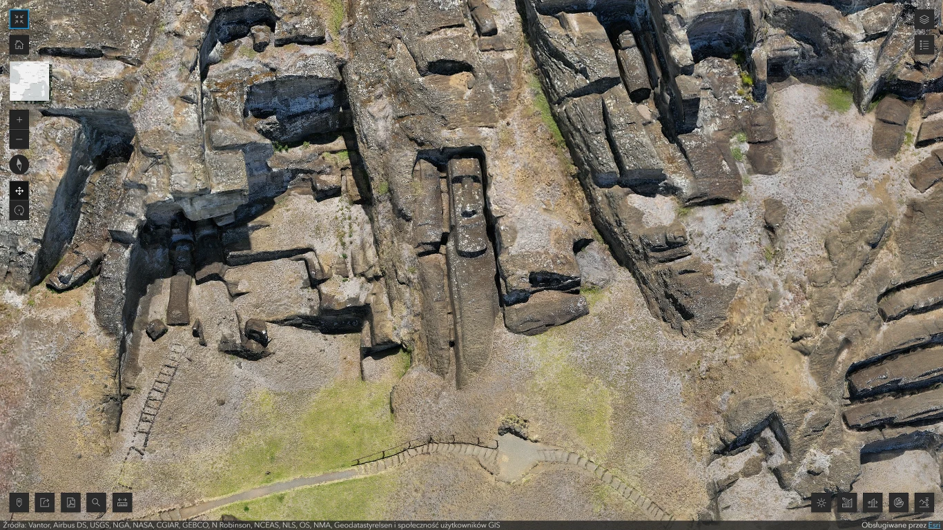 Kamienne ruiny i wykute w skale grobowce starożytnego miasta, widoczne z lotu ptaka. Skomplikowany układ przejść i schodów otacza wydrążone prostokątne komory, otoczone przez skaliste wzgórza.