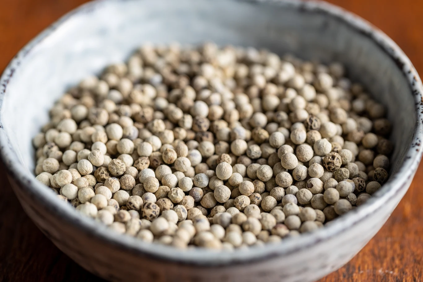 Biała miska wypełniona ziarenkami białego pieprzu, ustawiona na drewnianej powierzchni.