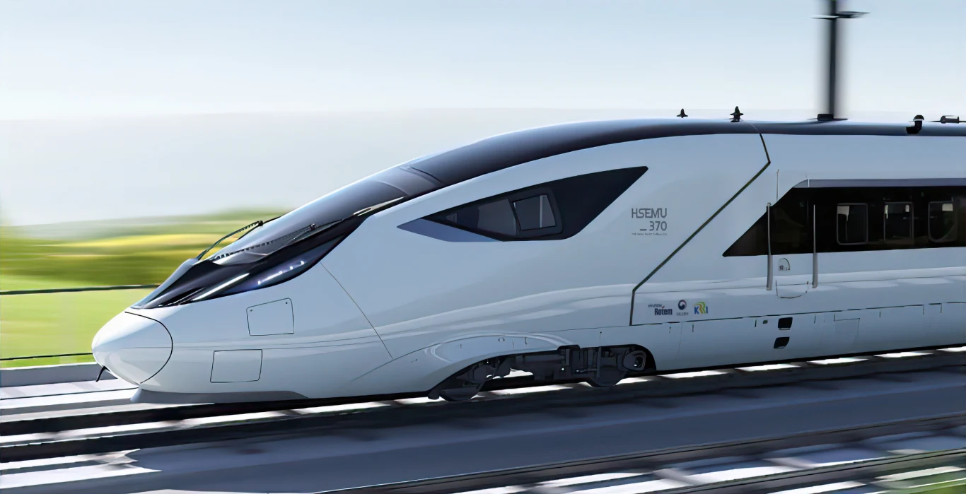 Nowoczesny biały pociąg dużych prędkości poruszający się po torach w jasny, słoneczny dzień; aerodynamiczny kształt, przeszklona kabina maszynisty i lekko rozmyte tło zielonych pól podkreślają szybkość i zaawansowanie technologiczne pojazdu.