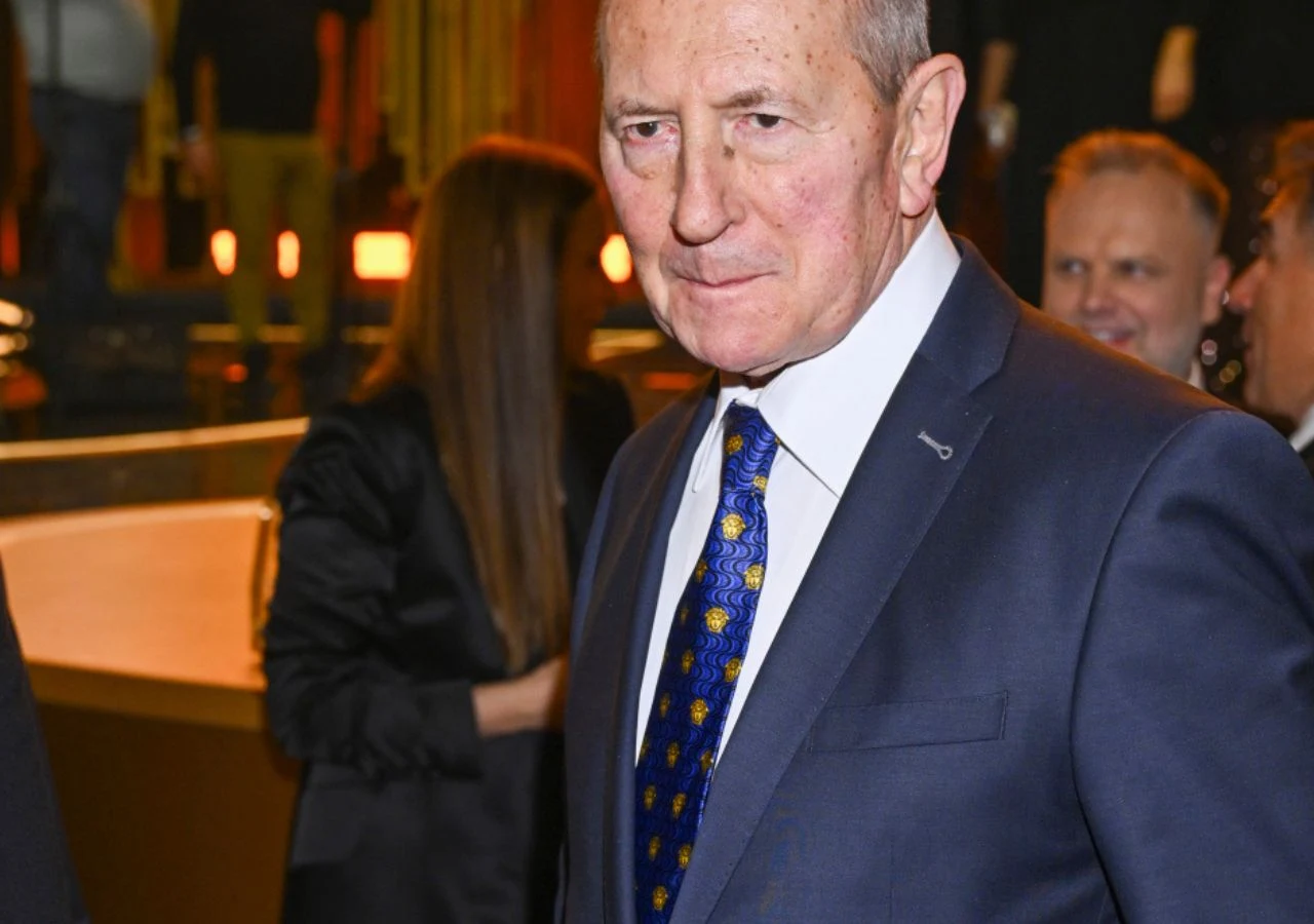 Włodzimierz Szaranowicz 2026 r. Mężczyzna w starszym wieku w eleganckim granatowym garniturze i niebieskim krawacie stoi w dobrze oświetlonym wnętrzu, w tle widoczne są inne osoby uczestniczące w wydarzeniu.