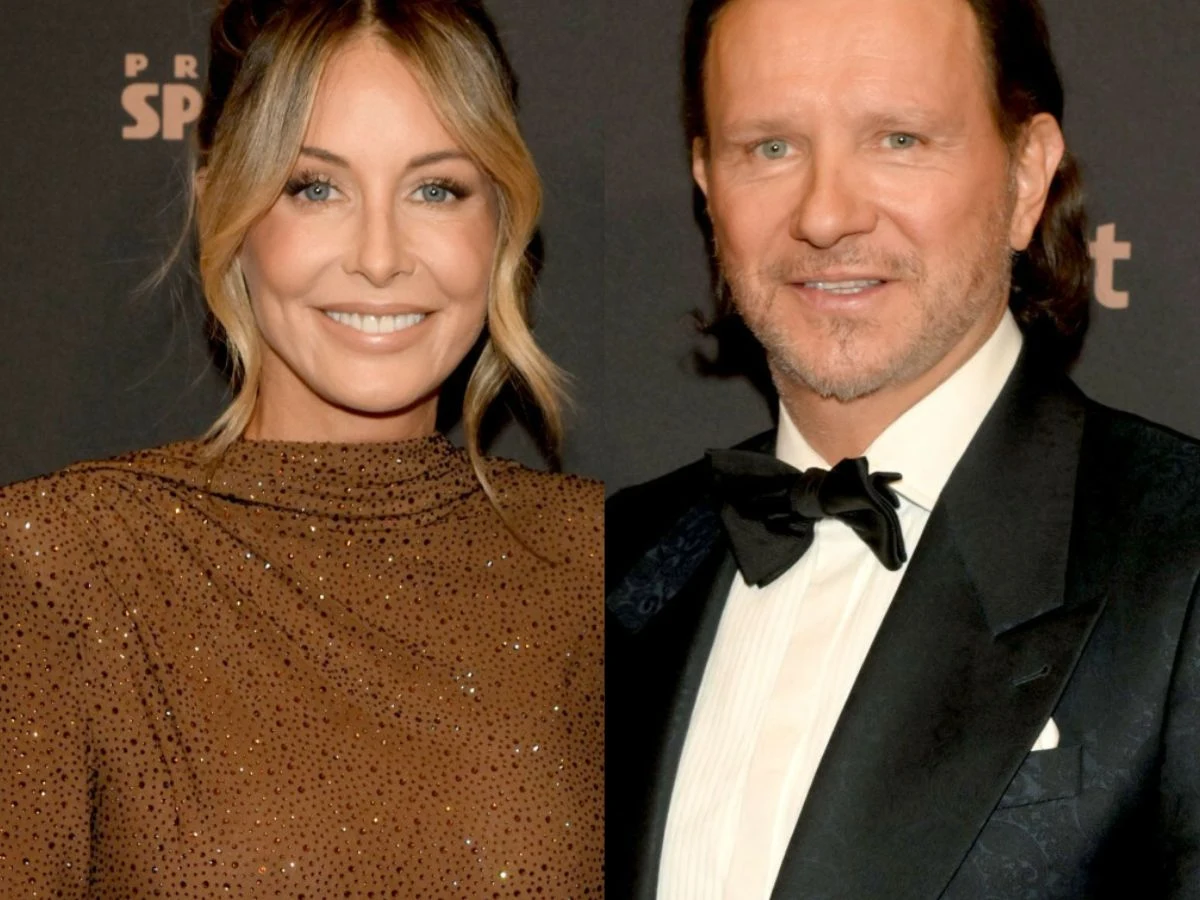 Małgorzata Rozenek, Radosław Majdan Elegancko ubrana kobieta w brązowej, połyskującej sukni i mężczyzna w czarnym smokingu, stojący obok siebie na tle ściany z napisem. Kobieta uśmiechnięta, jej włosy upięte w delikatny kok, mężczyzna z lekkim zarostem, w białej koszuli i muszce.