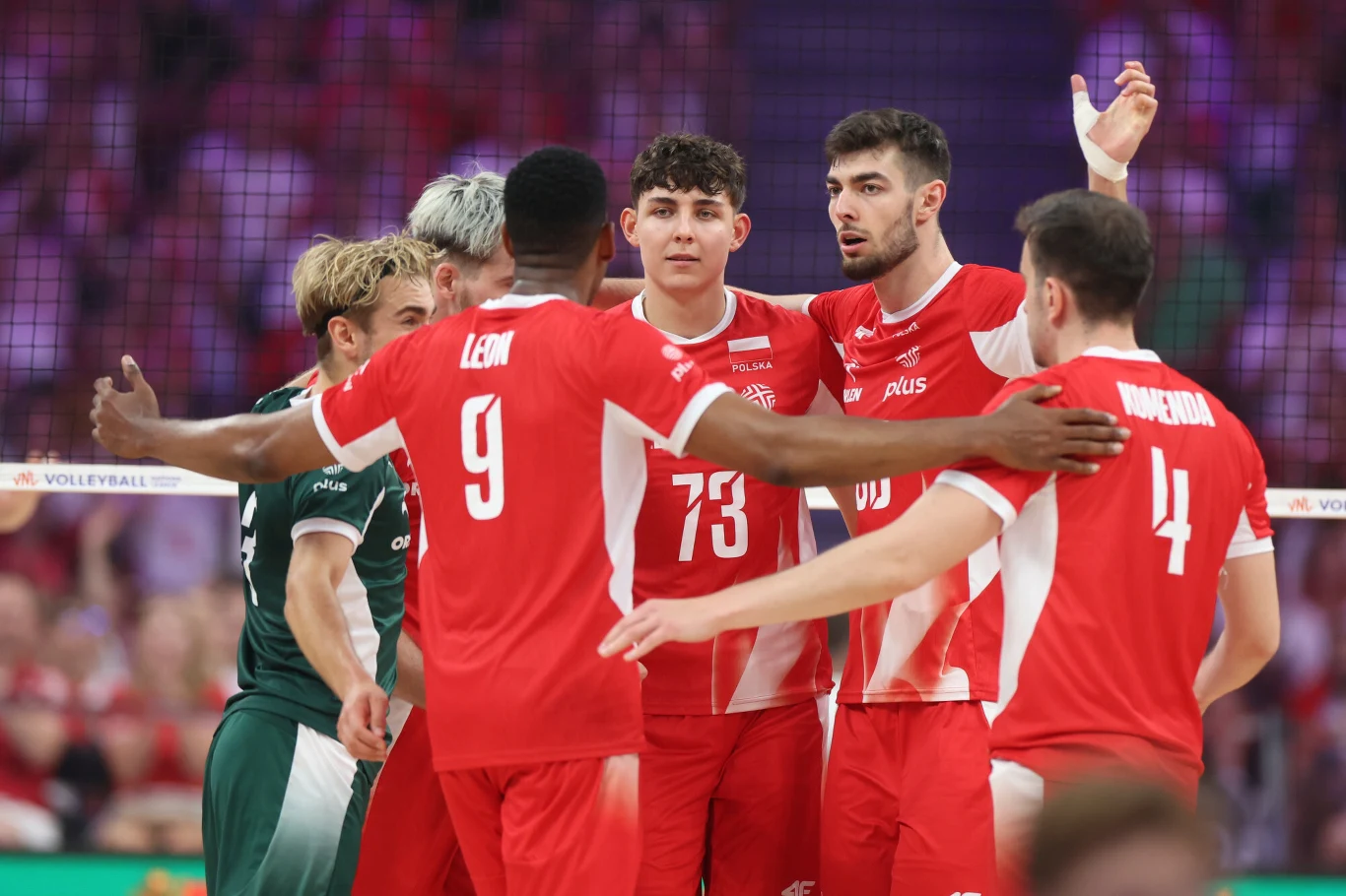 Kewin Sasak (drugi z prawej) wrócił do reprezentacji Polski Grupa siatkarzy w czerwono-białych strojach zgromadzona na boisku, zawodnicy wydają się świętować punkt lub konsultować strategię, w tle widoczni kibice i siatka.