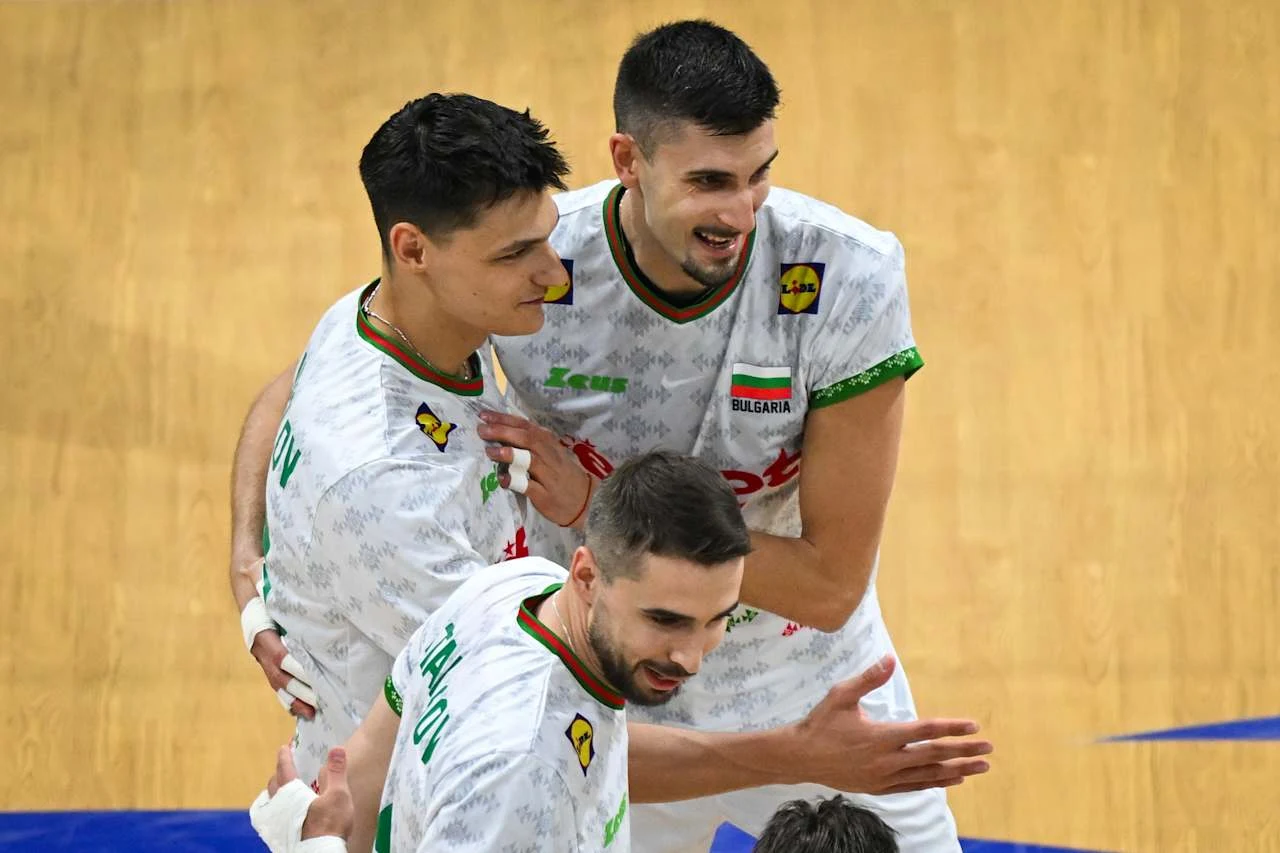 Aleks Grozdanow zdobył z Bułgarią medal MŚ na Filipinach Trzech siatkarzy w białych koszulkach z zielonymi akcentami oraz napisem Bułgaria świętuje zdobyty punkt na boisku do siatkówki, widoczna drewniana podłoga i fragment niebieskiej linii bocznej.