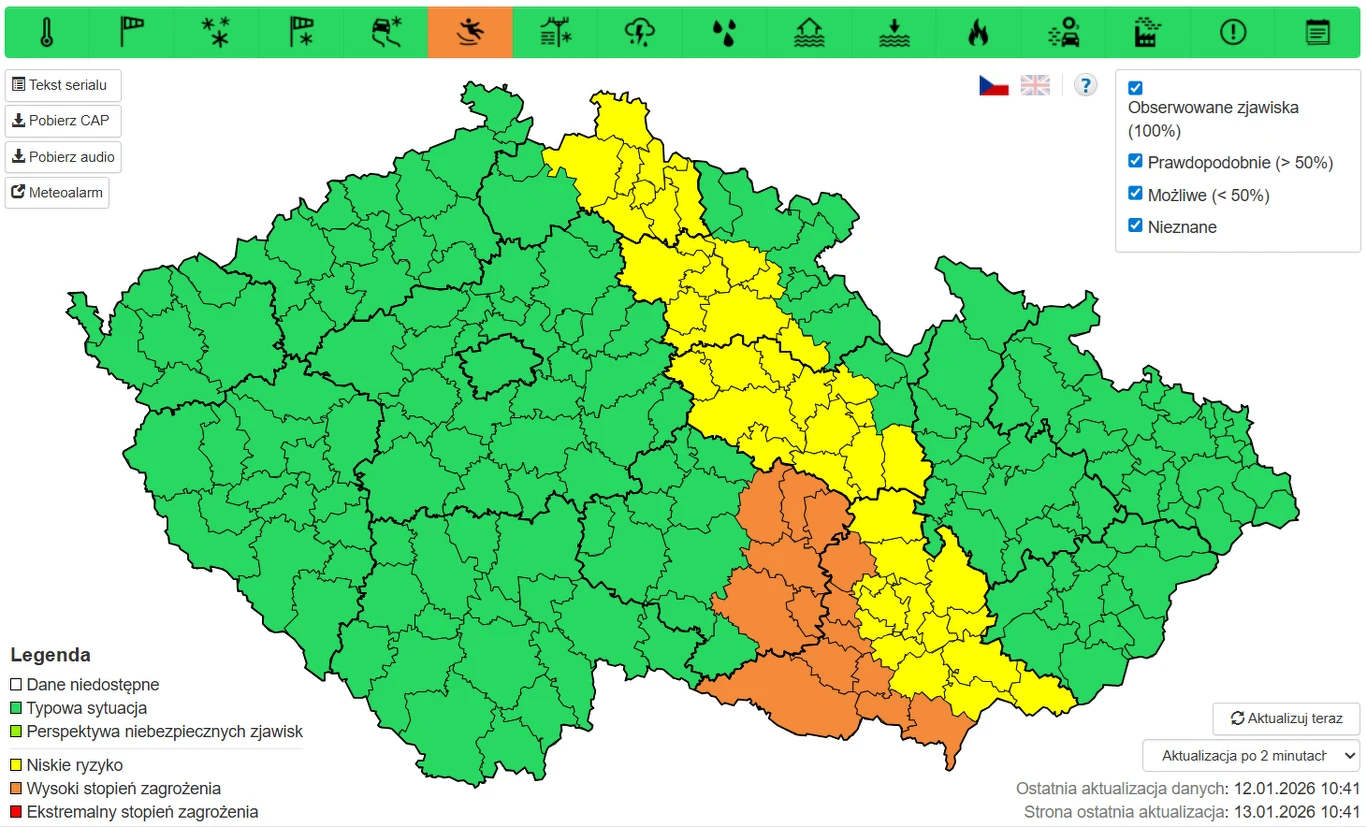 Kolorowa mapa Czech przedstawiająca podział administracyjny kraju z oznaczeniami stref zagrożenia. Zielone obszary oznaczają brak zagrożenia, żółte wskazują na wyższe ryzyko, a pomarańczowe na wysoki stopień zagrożenia. W legendzie wyjaśniono znaczenie...