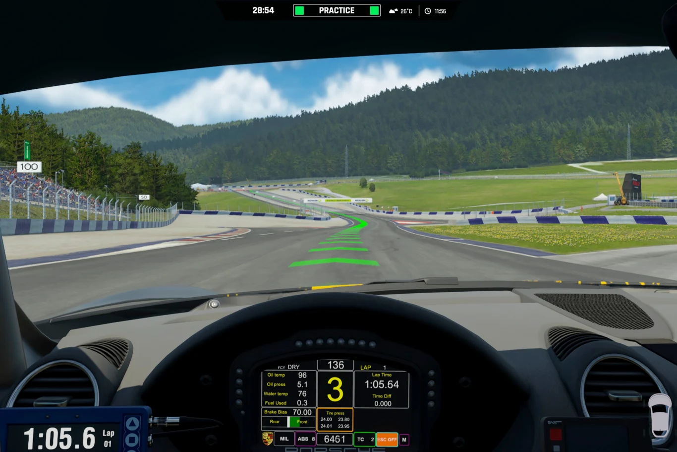 Widok z kokpitu samochodu wyścigowego na torze, panel z danymi samochodu widoczny na ekranie, tor wyznaczony przez zielone linie prowadzące, w tle zielone wzgórza i las, częściowo pochmurne niebo.