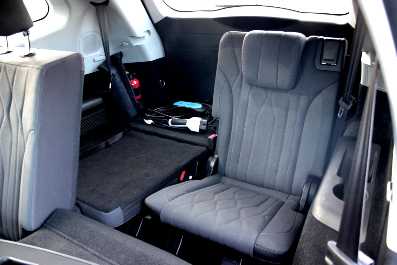 Tylna część wnętrza samochodu z rozłożonym oraz złożonym trzecim rzędem foteli, w przestrzeni bagażowej znajdują się akcesoria samochodowe, takie jak ładowarka i kabel.