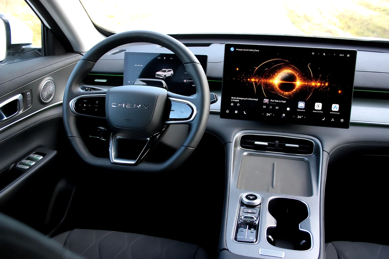 Nowoczesne wnętrze samochodu z dużym cyfrowym kokpitem, elegancką kierownicą i panelem sterowania z dwoma dużymi ekranami dotykowymi. Po lewej stronie widoczny cyfrowy zestaw wskaźników, środek z dużym ekranem multimedialnym. Minimalistyczna konsola ce...