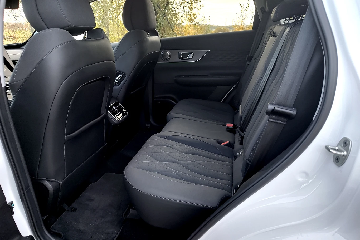 Tylny rząd siedzeń samochodu osobowego z ciemną tapicerką, widok na przestronne wnętrze i drzwi po prawej stronie lekko uchylone.