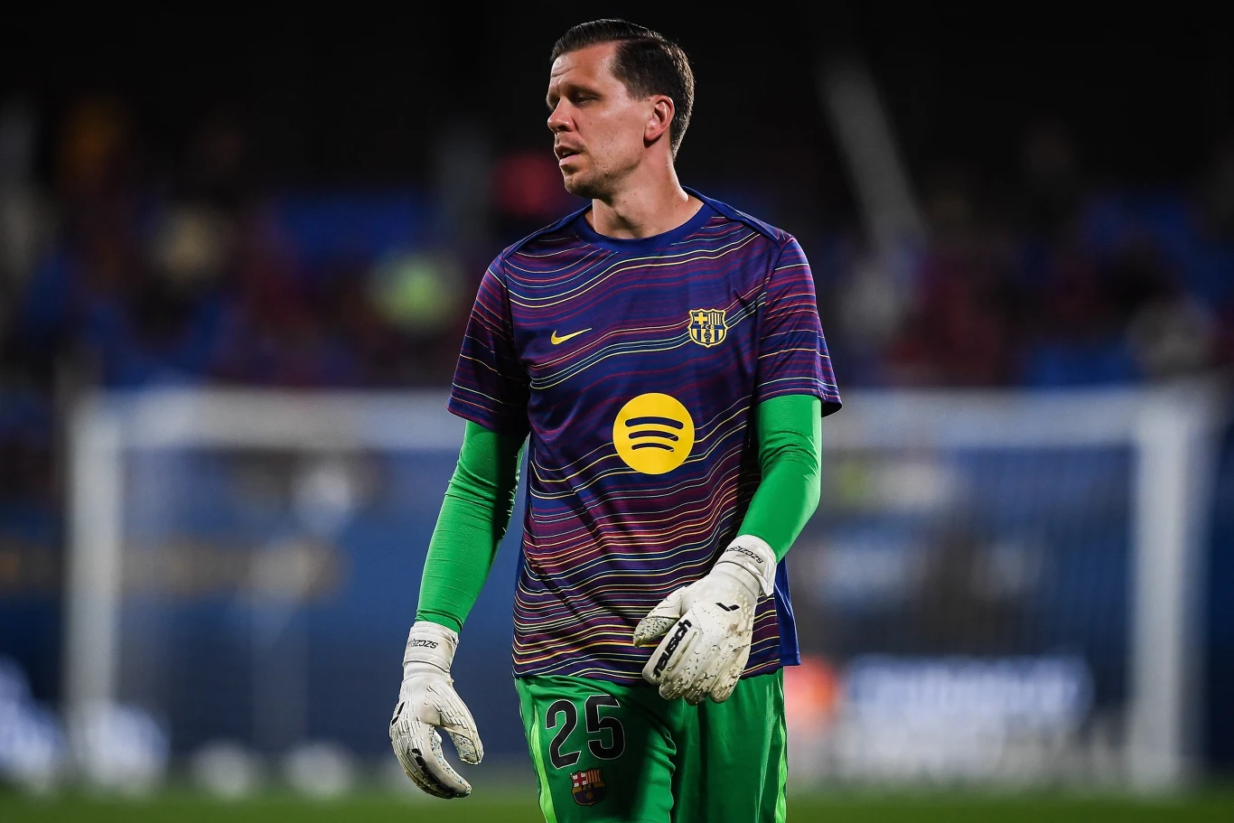 Bramkarz w stroju sportowym, z numerem 25 na spodenkach, w rękawicach bramkarskich, na tle nieostrego stadionu z widownią.