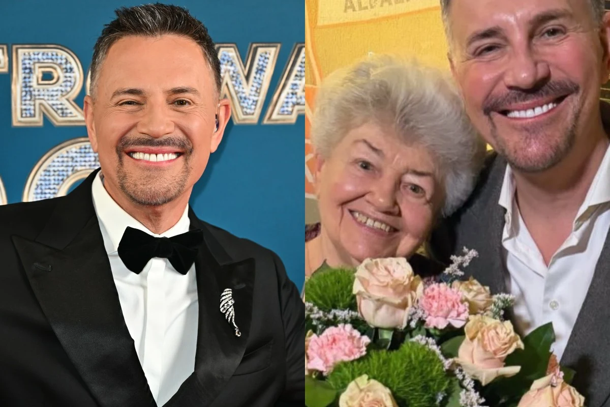 Mężczyzna w eleganckim smokingu z muchą po lewej stronie oraz starsza kobieta z bukietem jasnoróżowych róż i zielonych kwiatów pozująca z uśmiechniętym mężczyzną po prawej stronie.