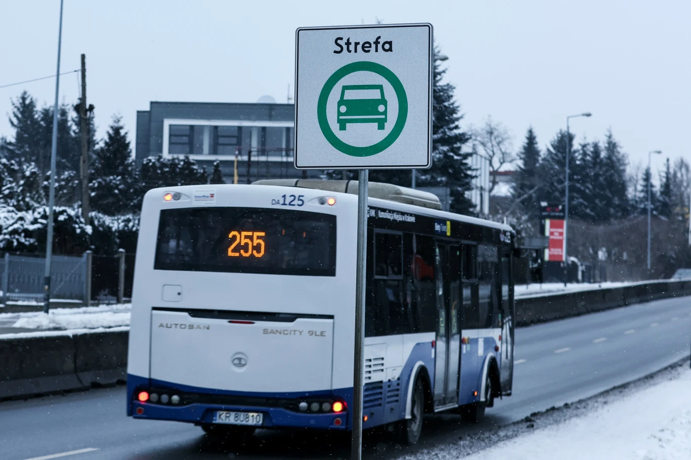 Strefa obowiązuje od stycznia 2026 r. Autobus komunikacji miejskiej z numerem linii 255 jedzie po ośnieżonej ulicy obok znaku oznaczającego strefę dla samochodów, w tle niska zabudowa mieszkalna oraz drzewa pokryte śniegiem.