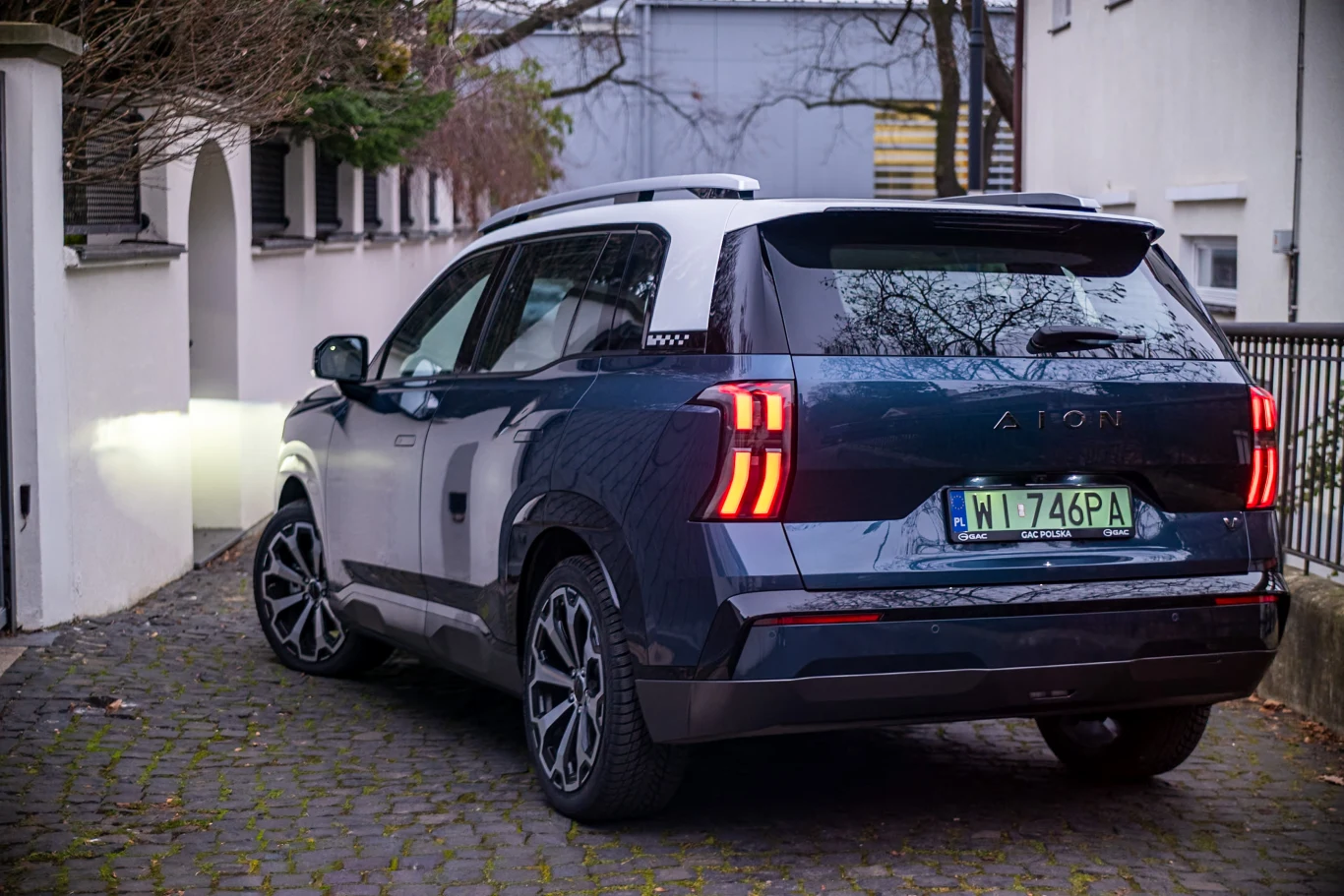 Ciemnoniebieski SUV z charakterystycznymi tylnymi lampami LED stoi zaparkowany tyłem do kamery na brukowanej uliczce wśród miejskiej zabudowy, z widocznymi rejestracjami i zimową aurą bez wyraźnych oznak śniegu.